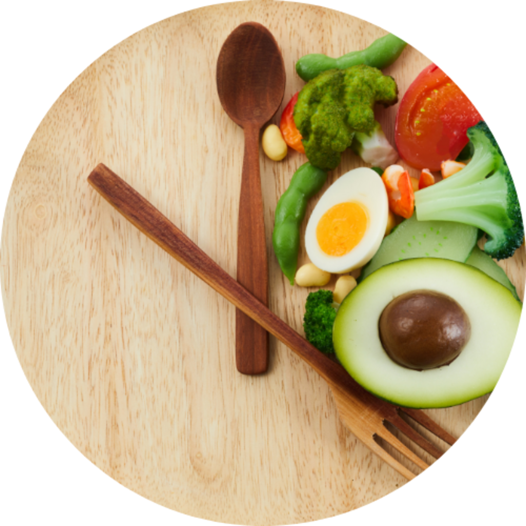 Clock made from wooden utensils beside vegetables, egg, and avocado